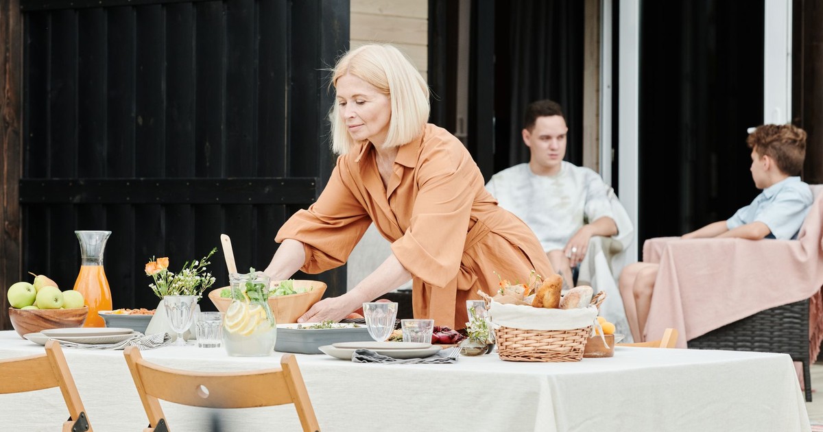 Woman preparing table for a family gathering outdoors. Elegant dining setup.