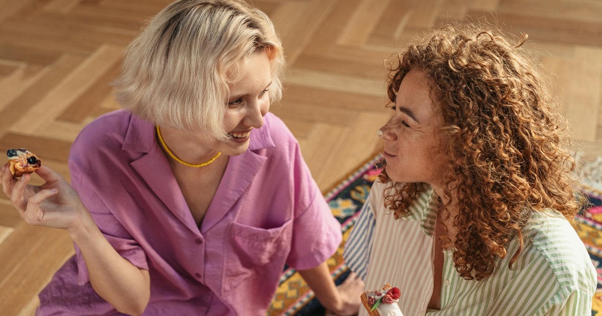 Two women sitting on the floor indoors, sharing desserts and enjoying a warm conversation.