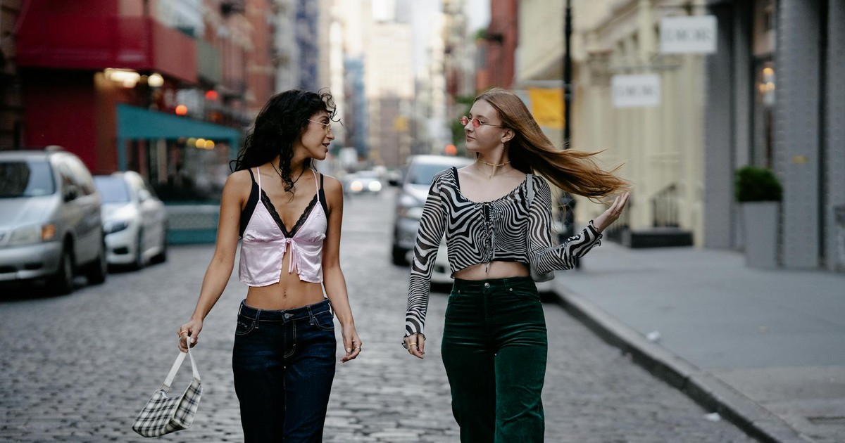 Two fashionable young women walking on a city street, showcasing trendy outfits and style.