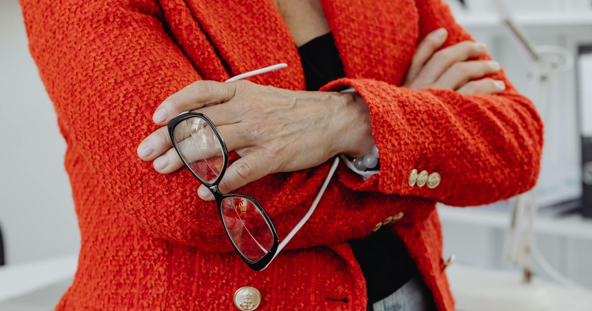 Close-up of a businesswoman in a red blazer holding eyeglasses, embodying confidence.