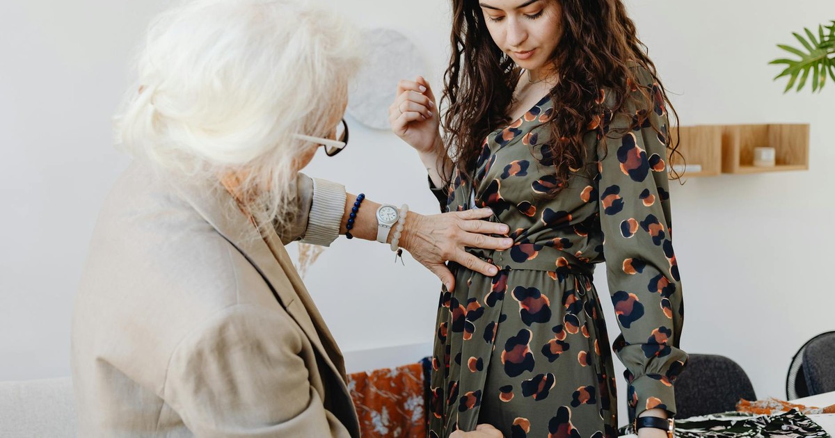Elderly woman adjusting granddaughter's dress indoors, showcasing a touching family moment.
