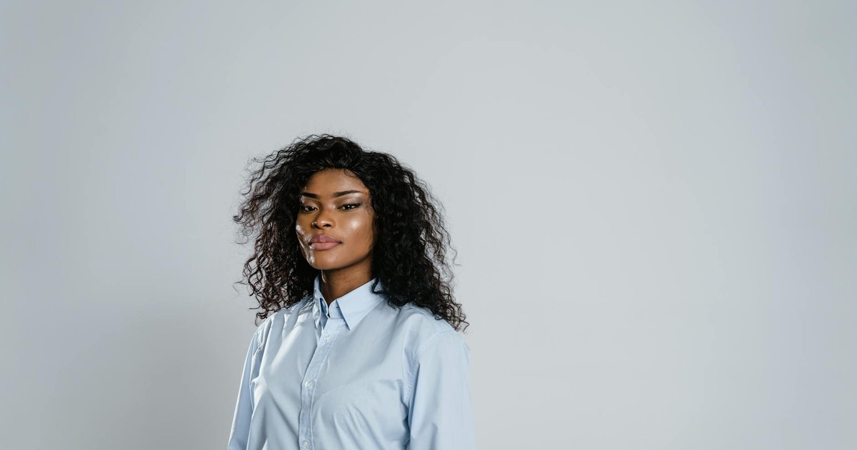 Professional portrait of a woman with curly hair in a blue shirt posing confidently.