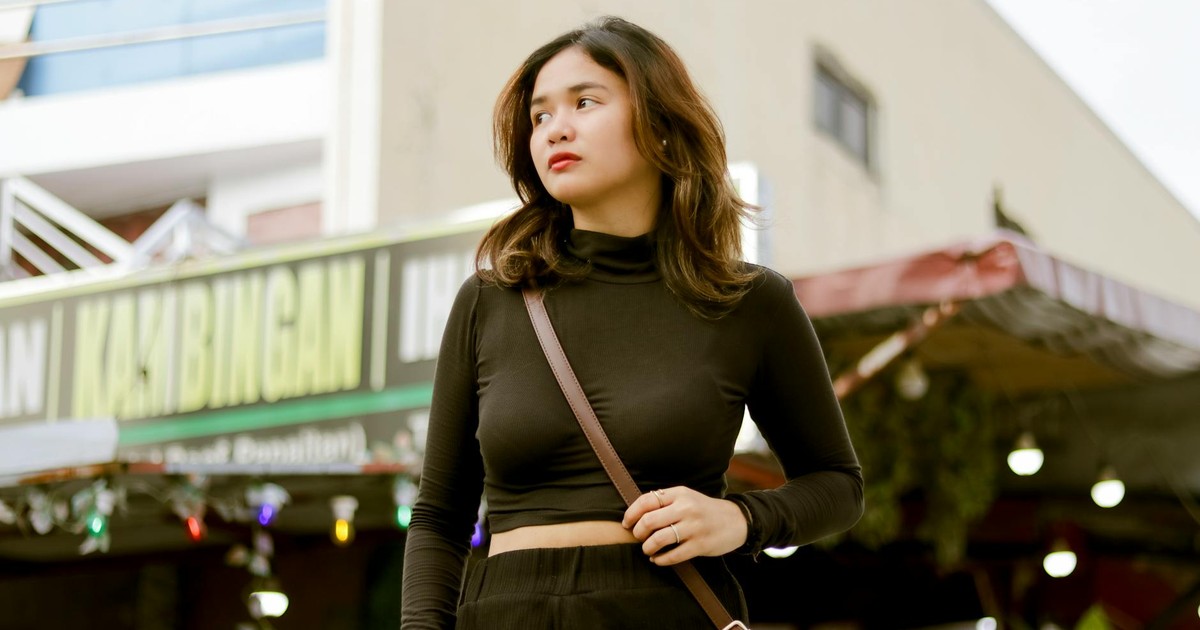 Stylish woman in black outfit confidently walking in an urban environment with a Kambingan restaurant backdrop.