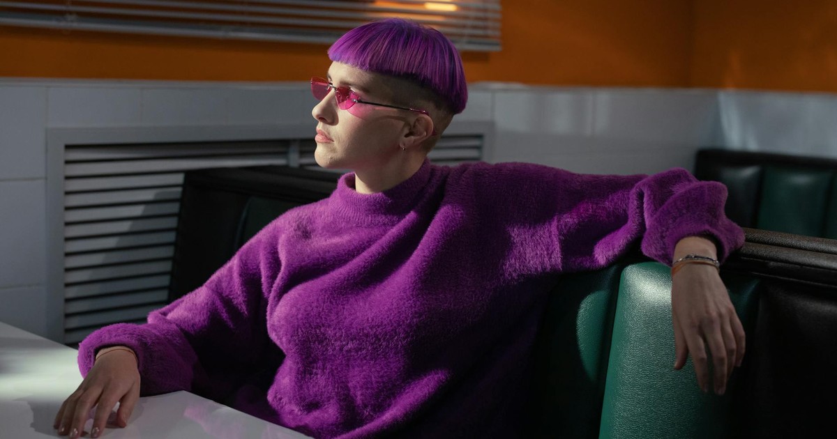 Woman with purple hair in stylish sweater at a café, embodying modern fashion.