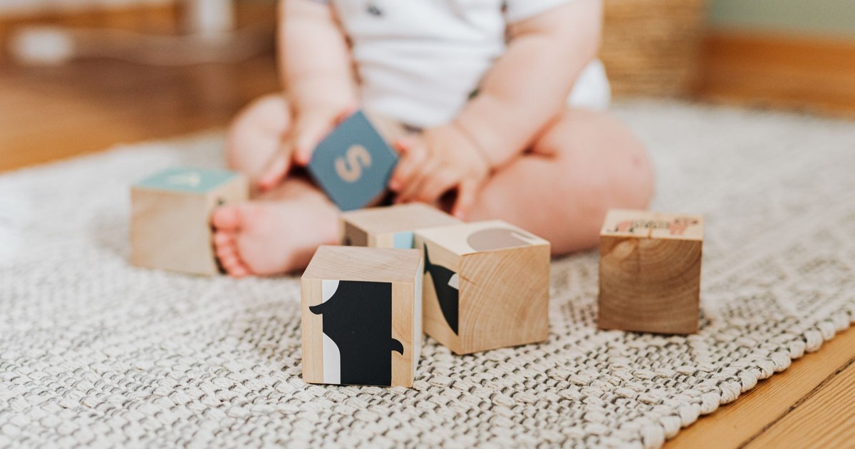 A baby engaging in play with wooden blocks on a textured carpet indoors.