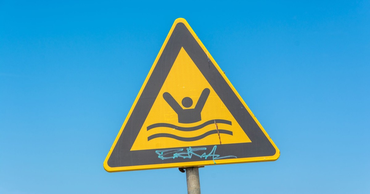 Yellow triangular warning sign for swimming area under a clear blue sky.