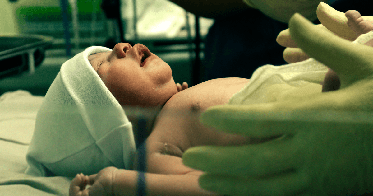 A newborn baby being gently handled by a nurse in a hospital setting.