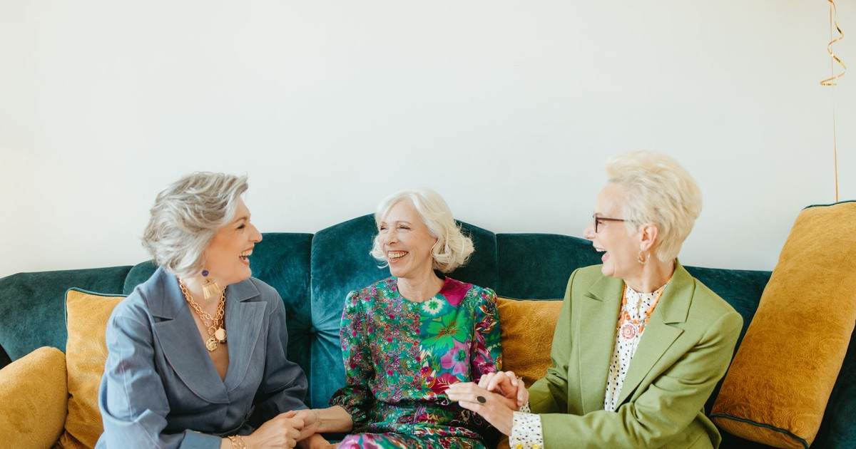 Three senior women laughing and bonding on a couch indoors