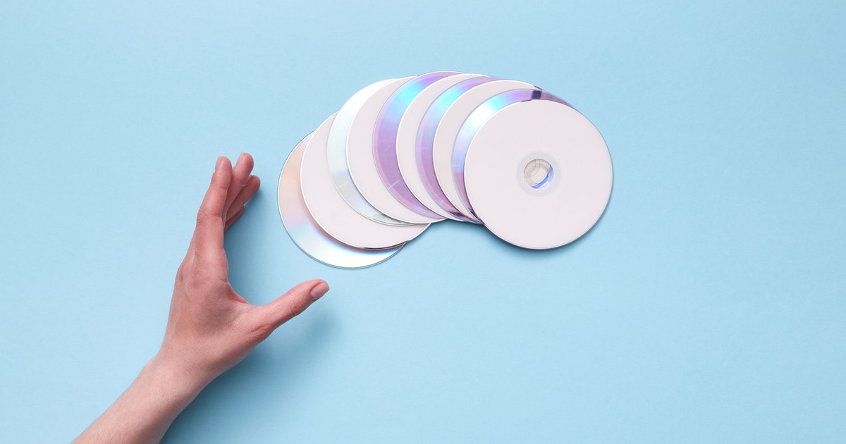 A hand reaching out to a stack of CDs on a blue backdrop, evoking nostalgia for retro technology.