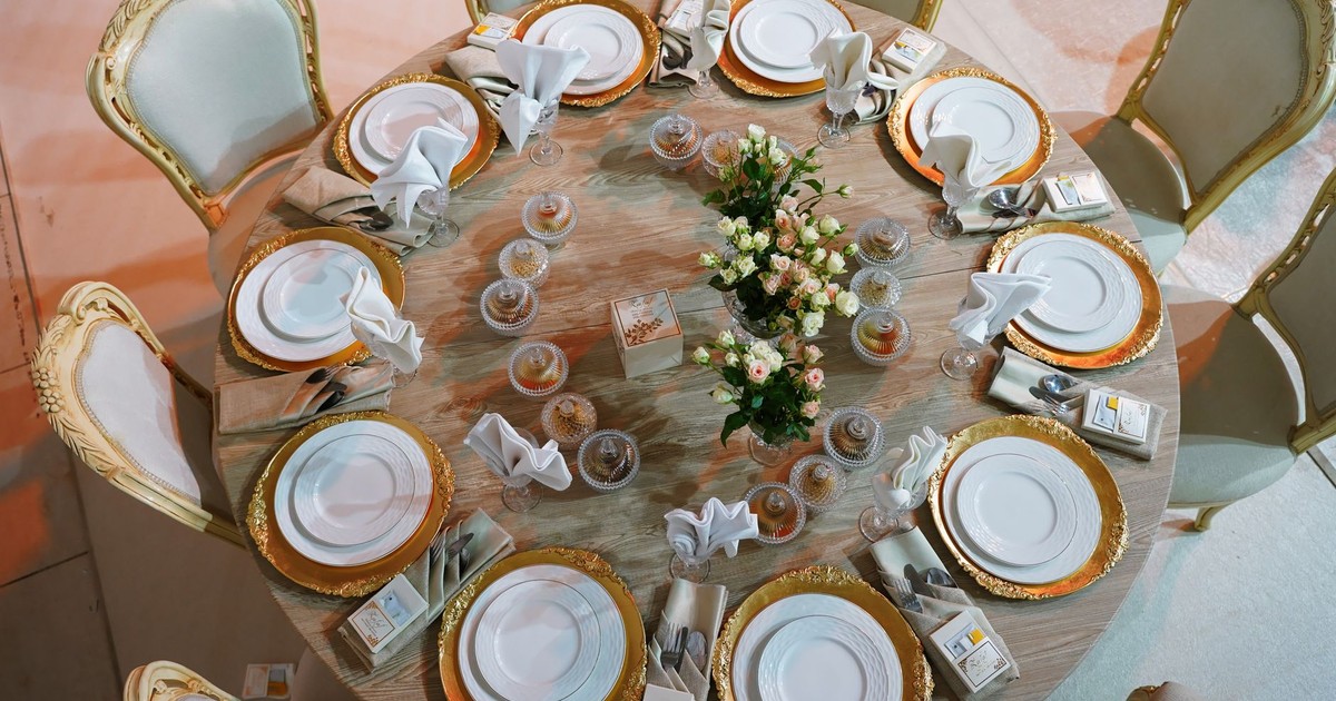 Luxurious round table with golden plates and roses, meticulously set for a wedding celebration.