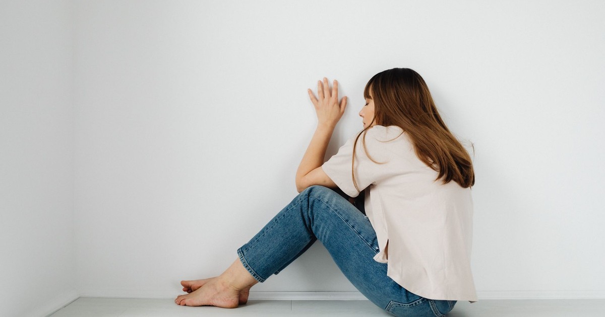 A contemplative woman sitting barefoot against a white wall, conveying solitude.