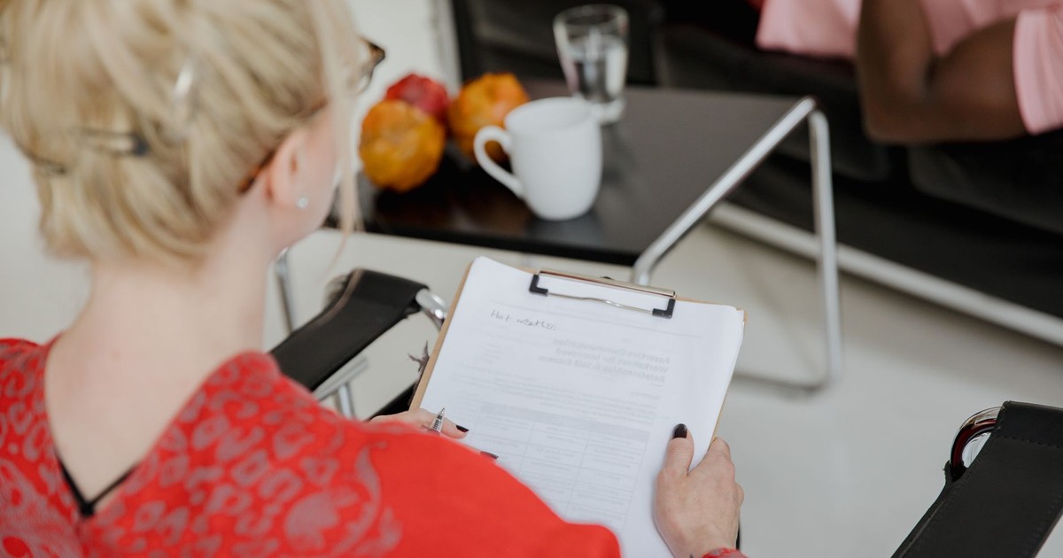A psychologist takes notes during a therapy session with a client, indoors.