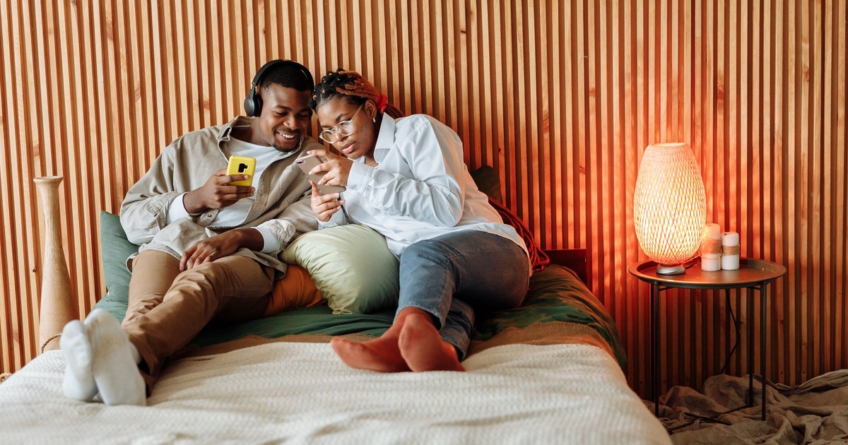 Couple enjoying a cozy moment with smartphones in a modern bedroom setting.
