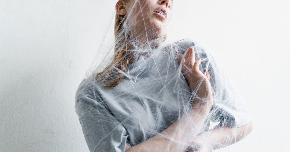 A woman enveloped in spider webs, representing anxiety and helplessness in an artistic conceptual shot.