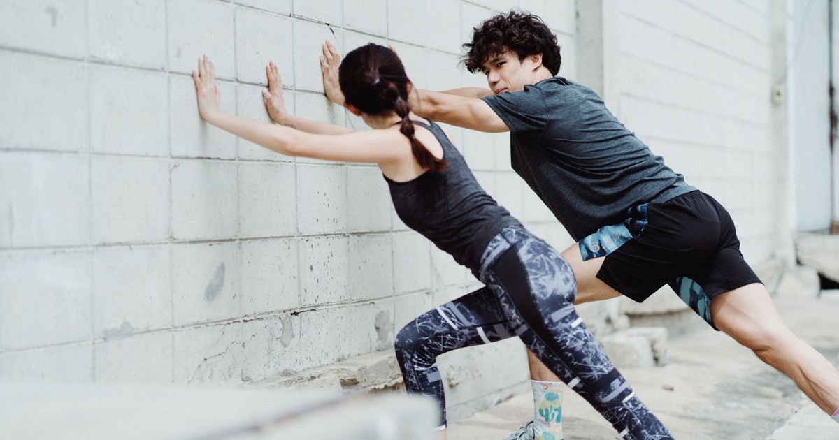 Man and woman stretching against a wall outdoors, showcasing athletic strength and teamwork.