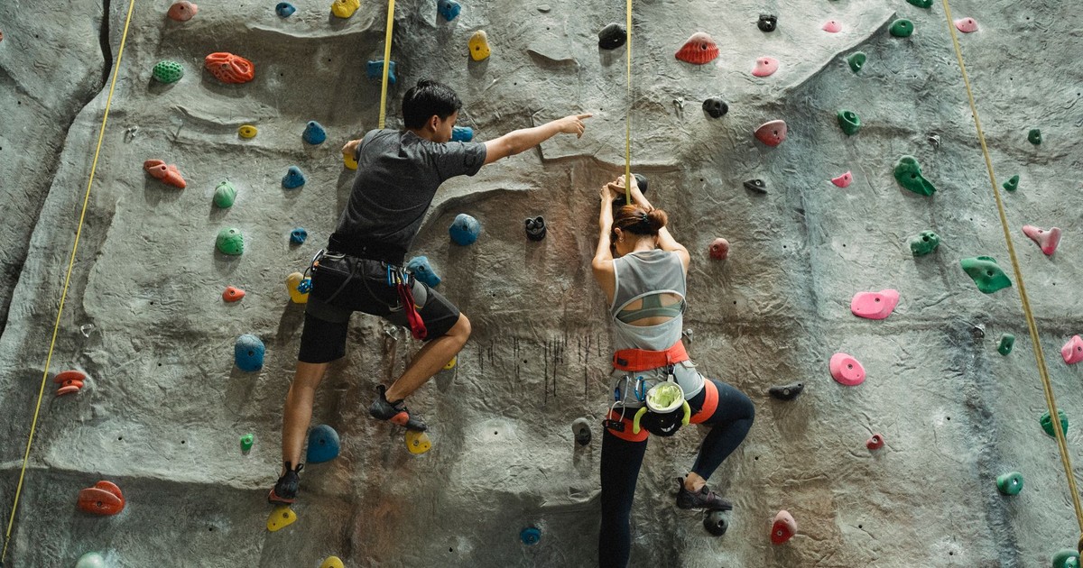 Back view of faceless mountaineers in sportswear with belay training climbing on wall