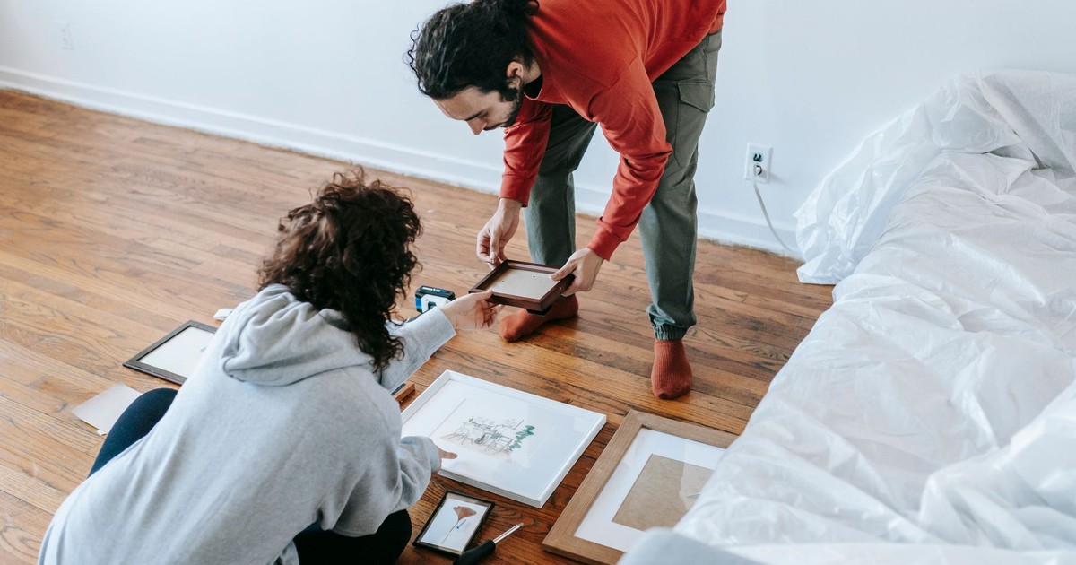 A couple collaborates on arranging picture frames in their new living space, creating a cozy atmosphere.