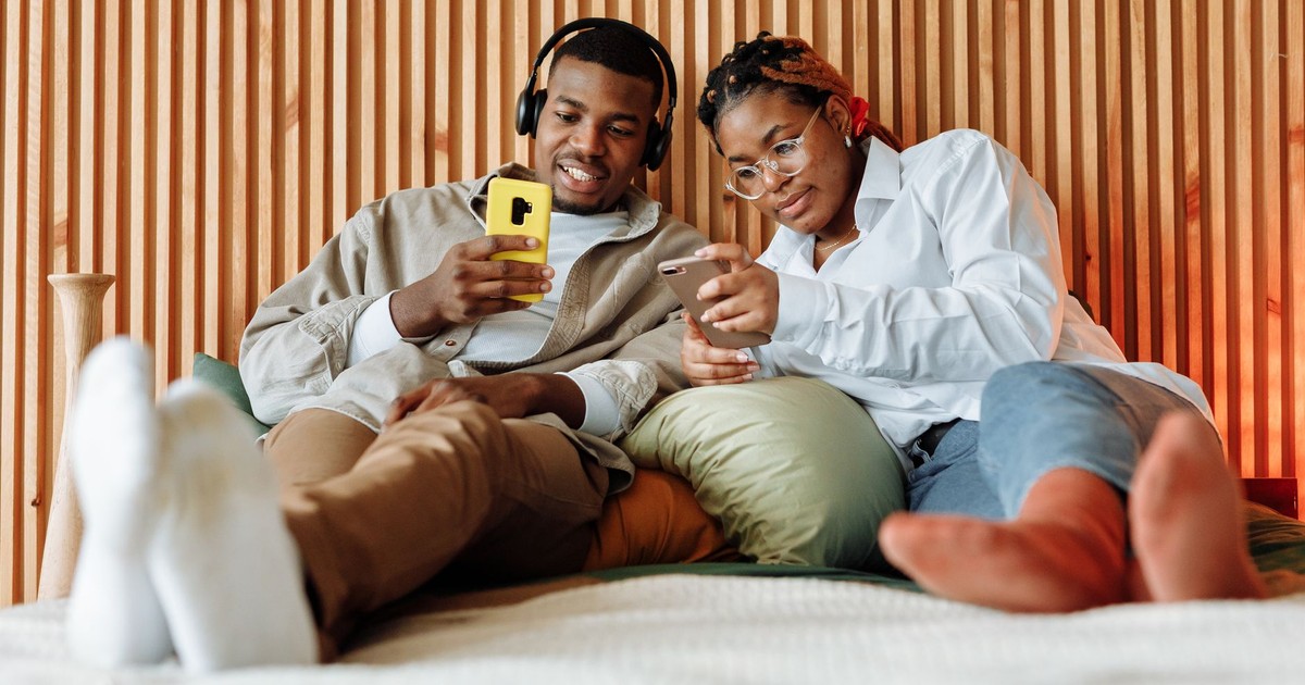Young couple sitting on a bed, enjoying smartphone content together in a cozy, modern setting.
