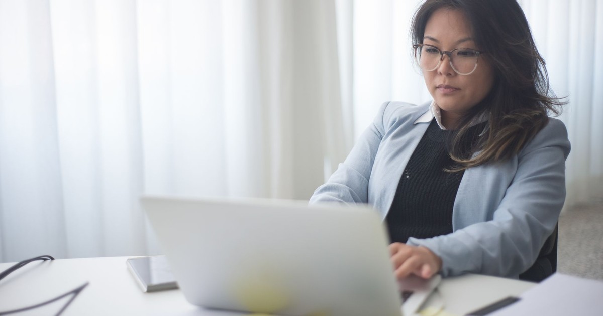 Focused businesswoman in office working on laptop with documents on the desk.