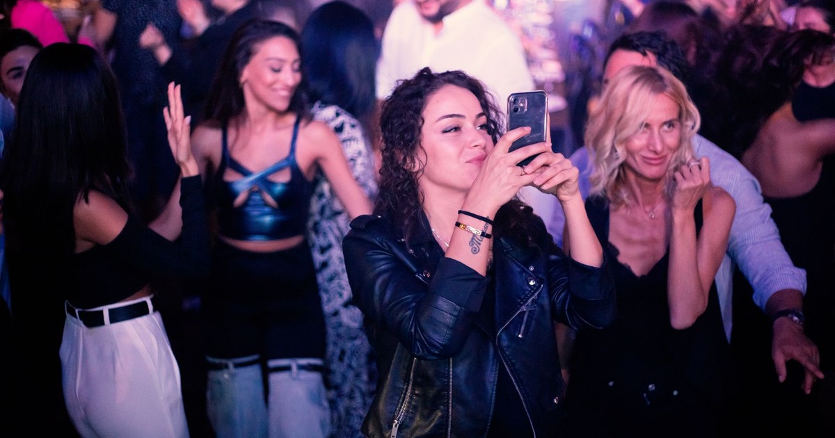 Energetic nightlife scene with people dancing and taking photos in a nightclub.
