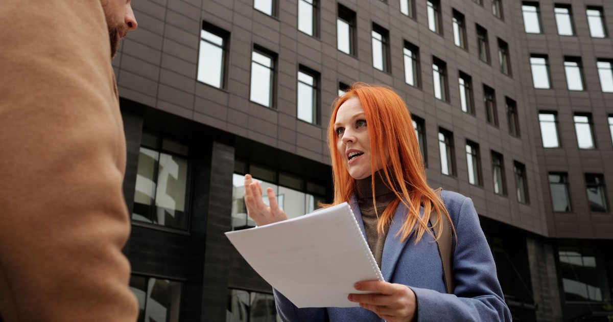 Professional woman and colleague in conversation holding documents outdoors