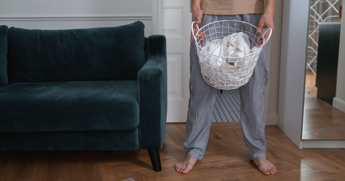 A man stands in a living room holding a laundry basket with clothes.
