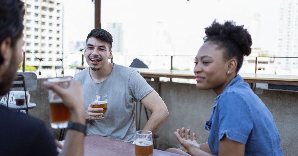 Group of friends socializing and enjoying drinks at a rooftop bar with a city view.