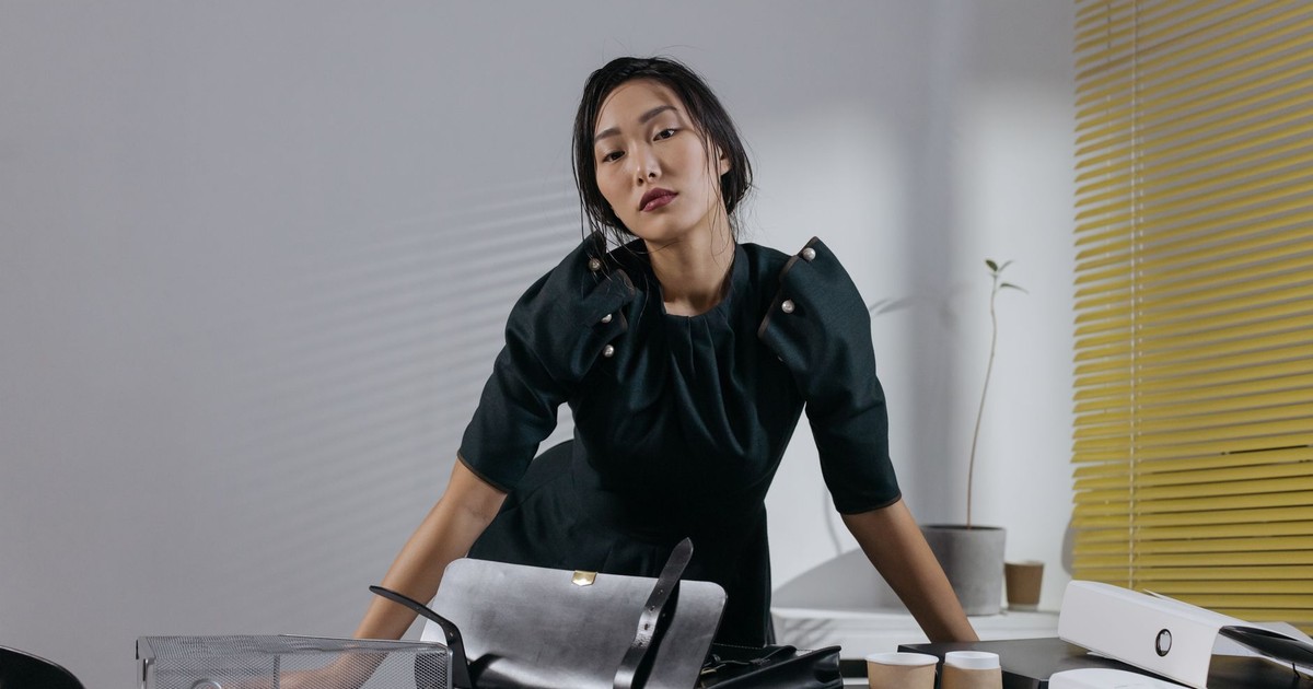 Asian woman in black dress posing confidently in a stylish office setting with modern decor.
