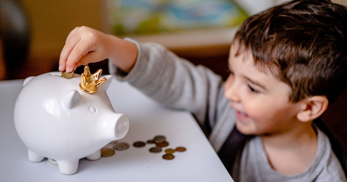 Young boy smiling while saving money in a crowned piggy bank, demonstrating financial responsibility.