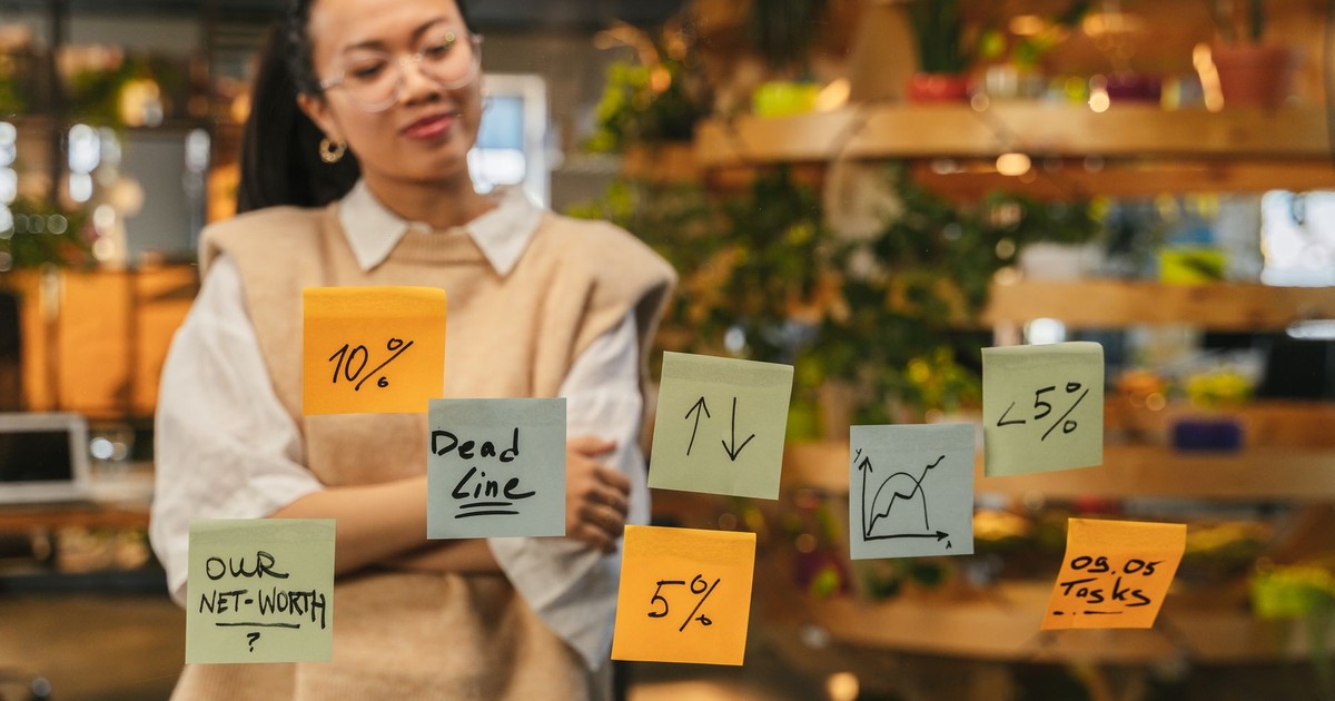 Woman analyzing sticky notes with graphs and deadlines in modern office space.