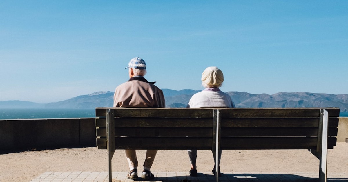 man and woman sitting on bench facing sea