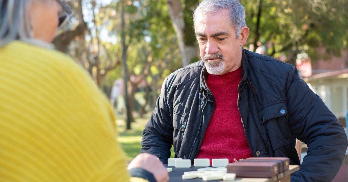 Senior couple playing dominoes outdoors in a sunny park, enjoying leisure time together.
