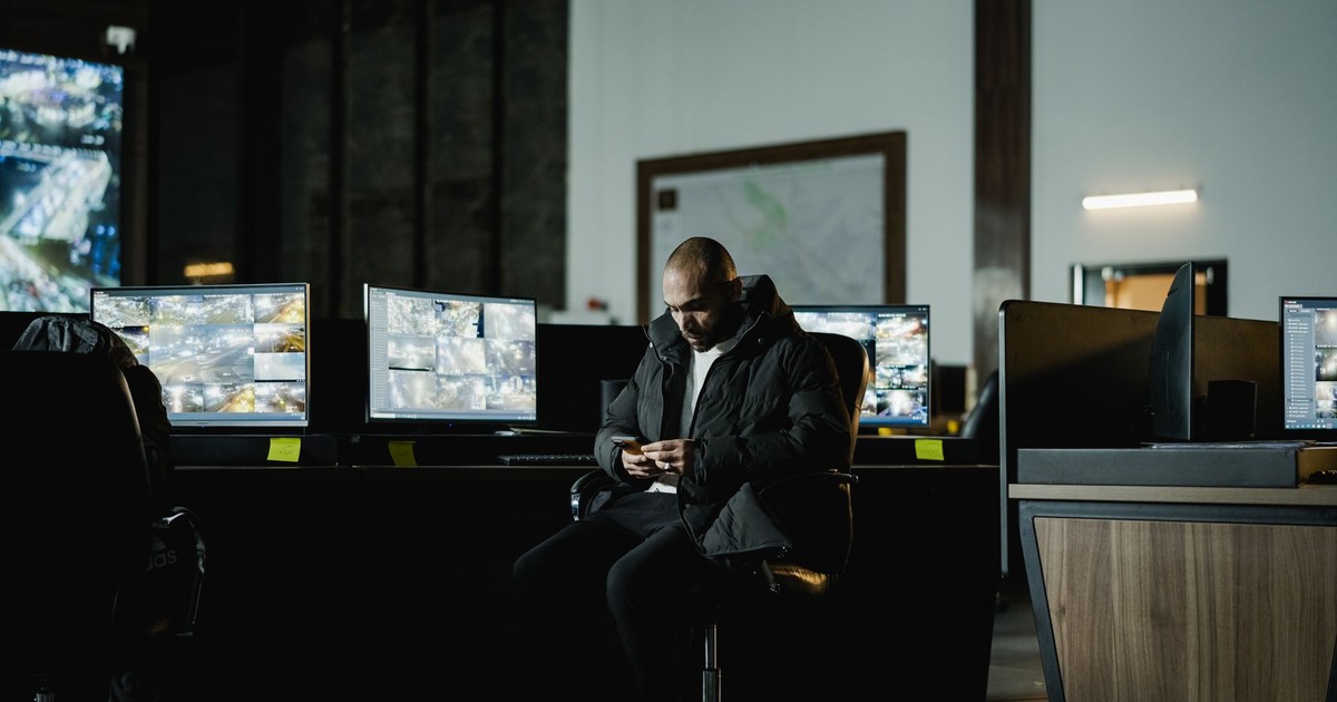 Security officer seated in a dimly lit control room, analyzing multiple surveillance screens.