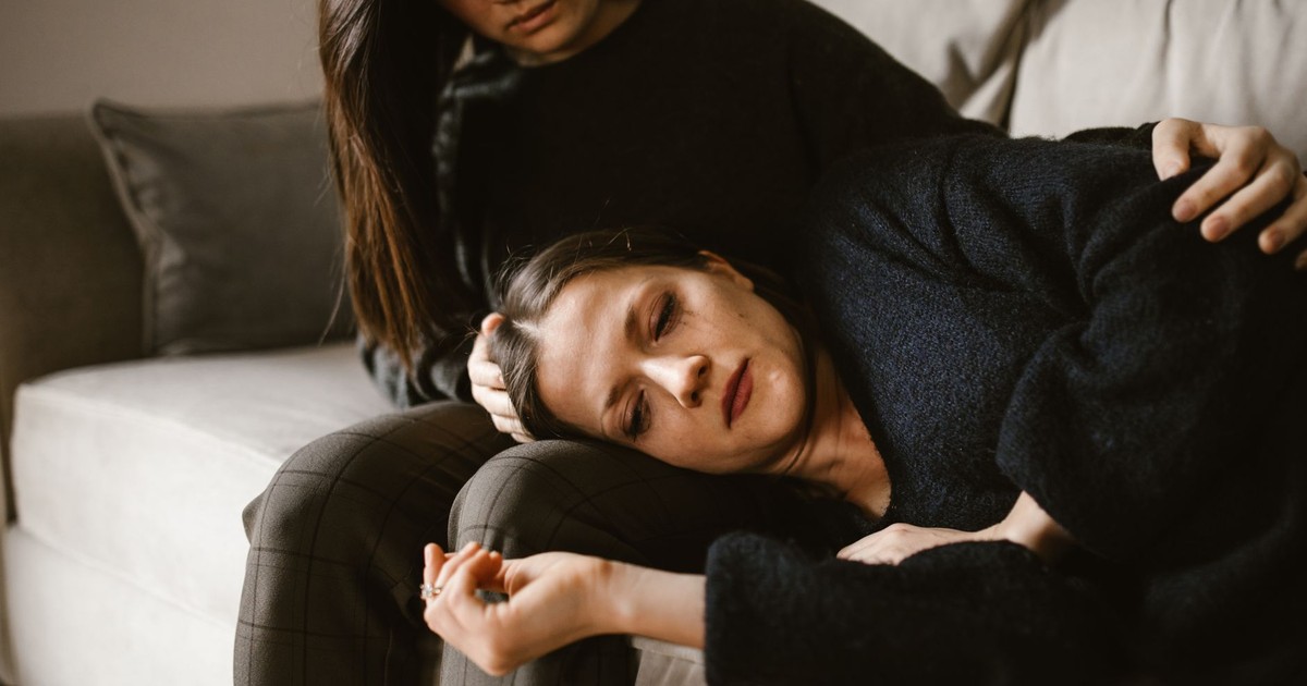 Two women on a couch, one comforting the other, depicting empathy and support.