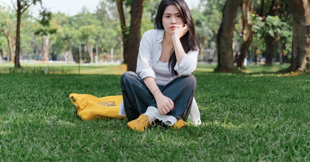 A young woman sitting on grass in a sunny park, enjoying a peaceful moment.