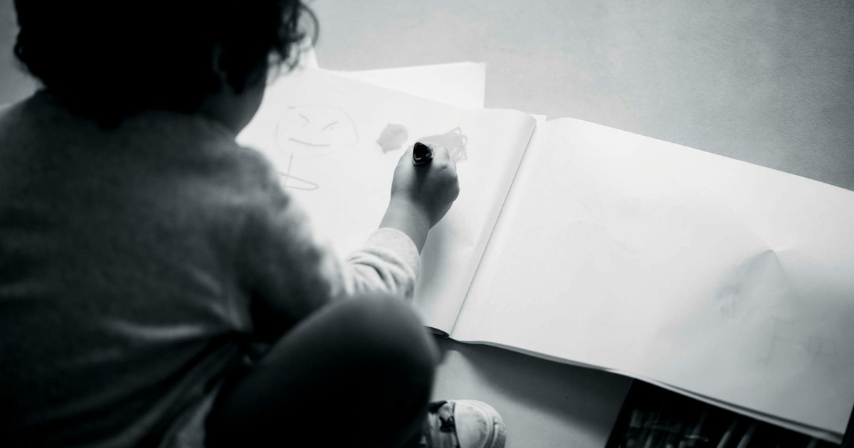 A child sketching on a large notepad with art supplies nearby, captured in black and white.