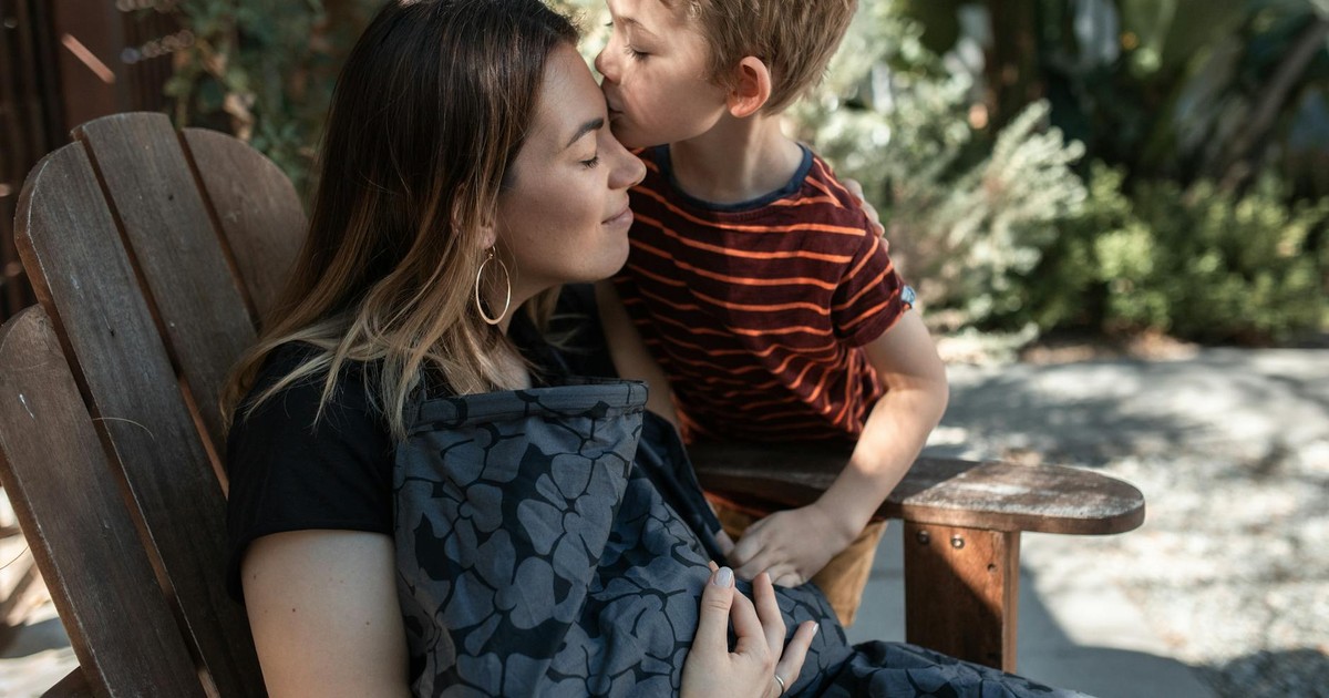 A tender moment as a young boy kisses his mother's forehead while sitting outside.