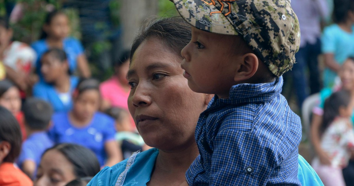 A mother holding her child amidst a crowd at an outdoor event.