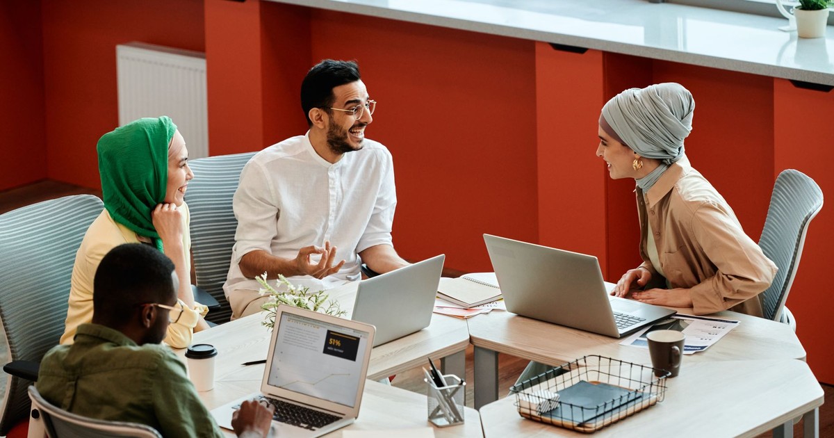 A group of diverse coworkers engaging in a collaborative discussion with laptops in a modern office setting.