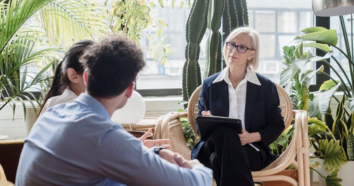 A counselor conducting a therapy session with a couple in a plant-filled room.