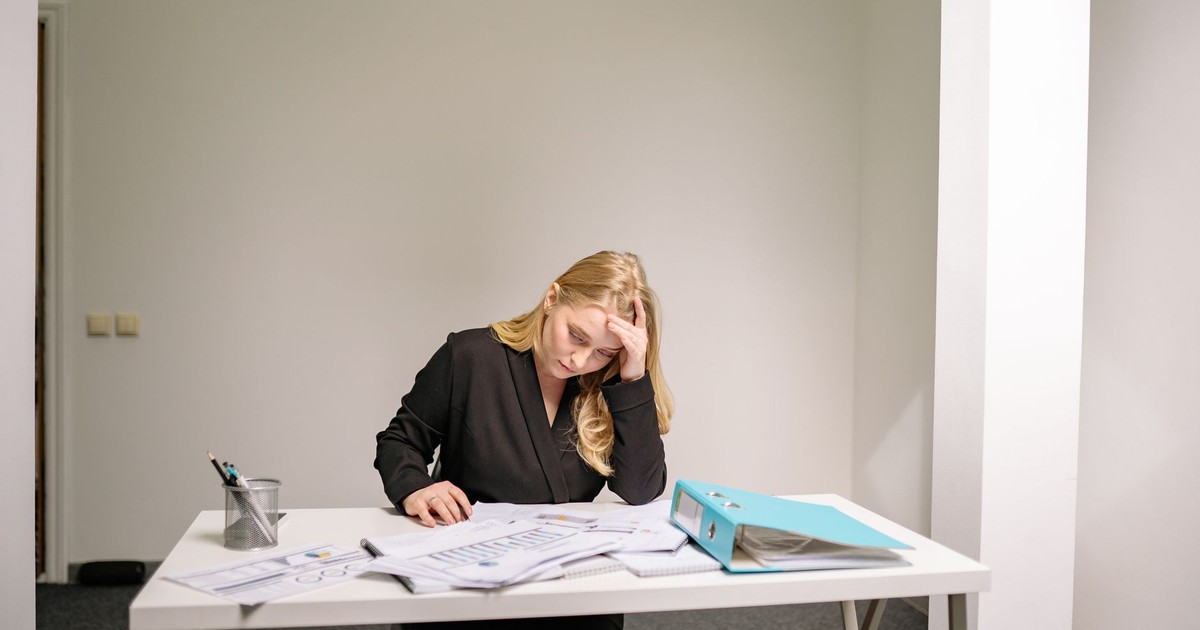A stressed businesswoman reviewing documents at her desk, overwhelmed by paperwork.