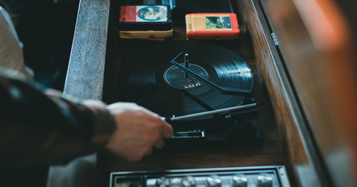 Close-up of a vintage turntable playing a vinyl record with visible hand adjusting. Classic music setup indoors.