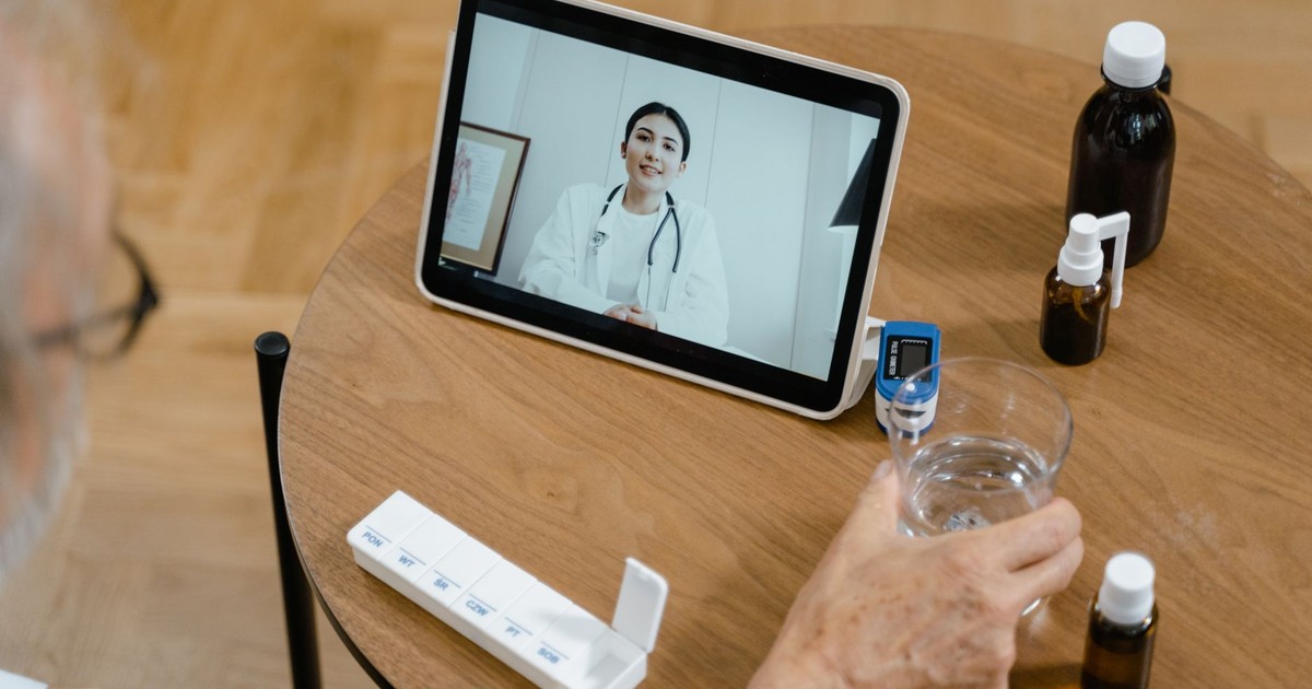 Senior adult having a virtual doctor consultation on a tablet with medications on the table.