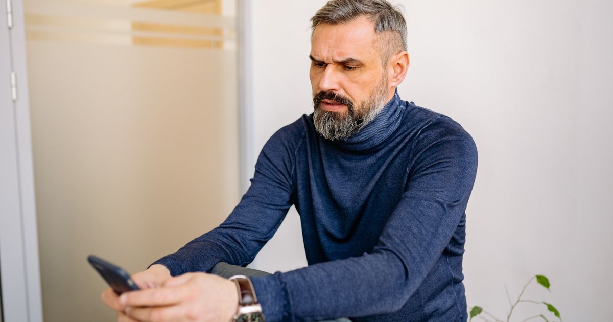 Serious middle-aged man sitting and using a smartphone indoors.