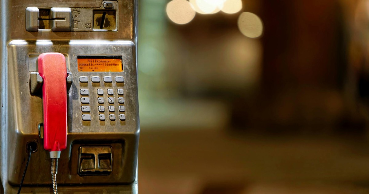 Vintage public telephone with red handset in an urban setting, blurred bokeh background.