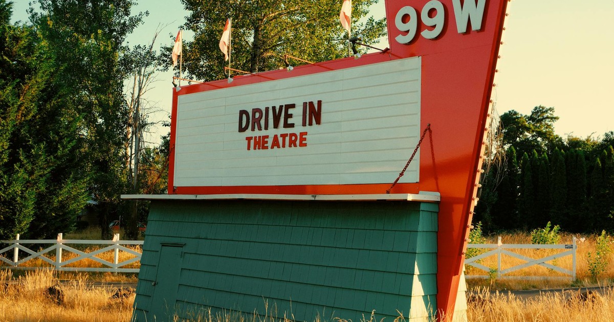 Vintage drive-in theatre sign in the countryside surrounded by trees and grasses.