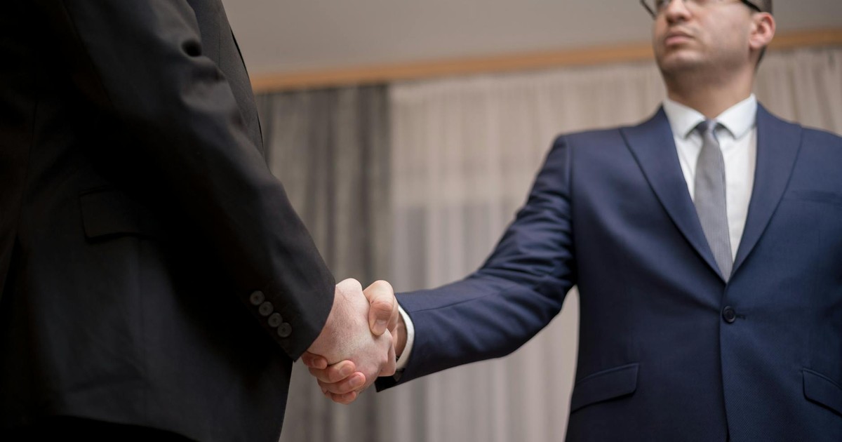 Two businessmen in formal attire shaking hands during a meeting.