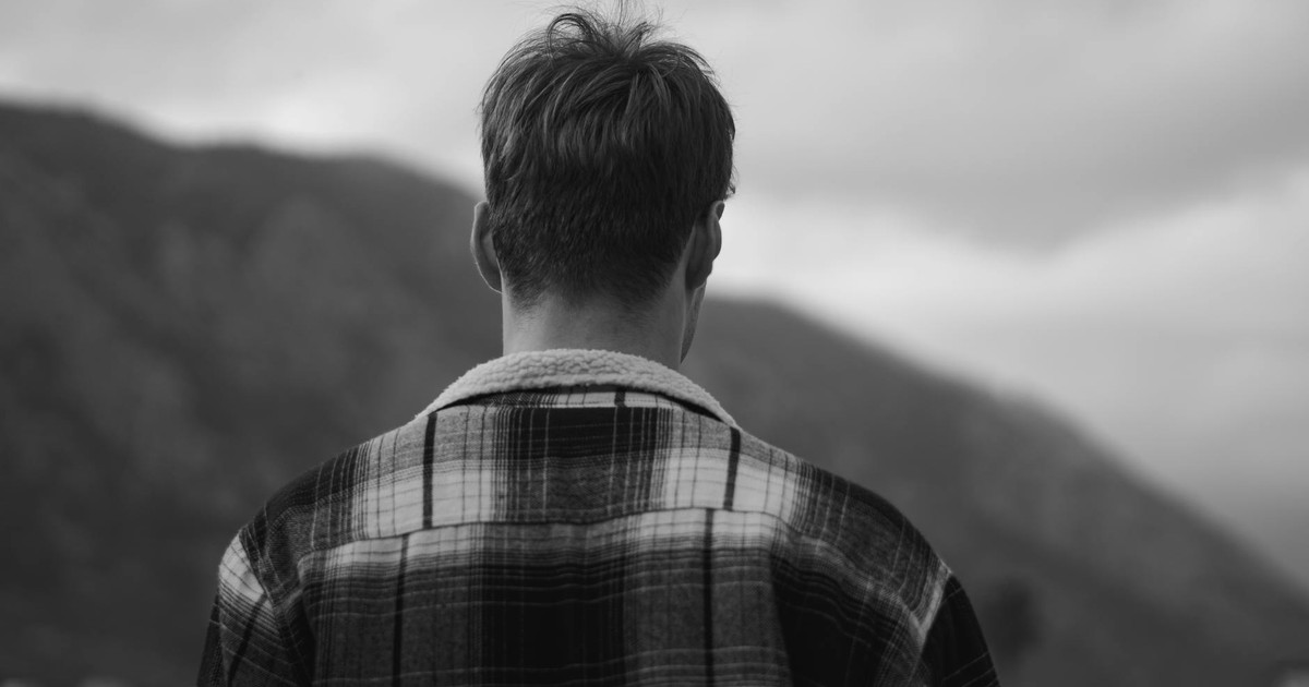 Black and white photo of a man in a checkered jacket looking at mountains.