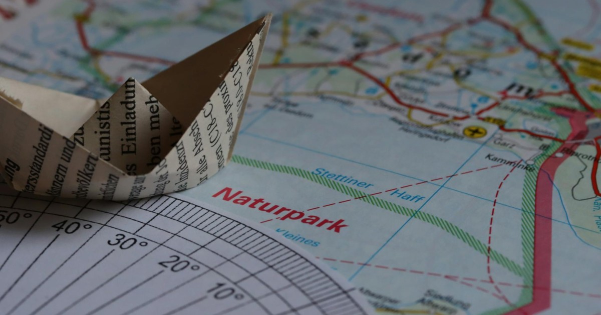 A paper boat sits on a map navigating a nature park, symbolizing travel and adventure.