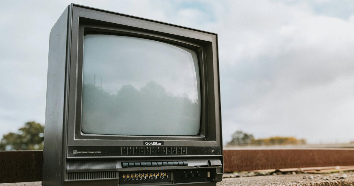 Black old fashioned obsolete television with reflection on screen placed on concrete railing against cloudy ski on street on blurred background